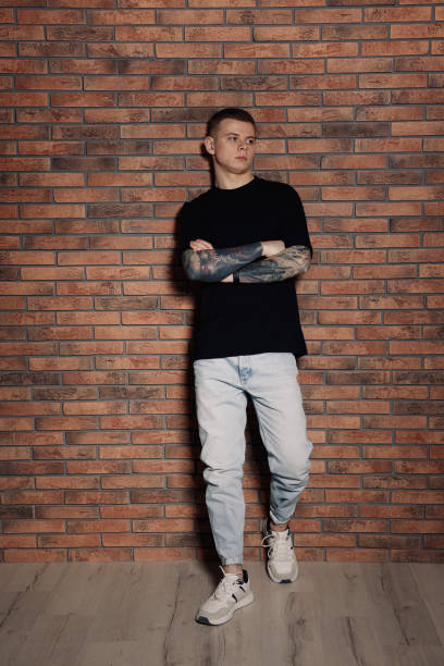レンガの壁の近くに入れ墨をした若者 - tattoo t shirt brick wall portrait ストックフォトと画像