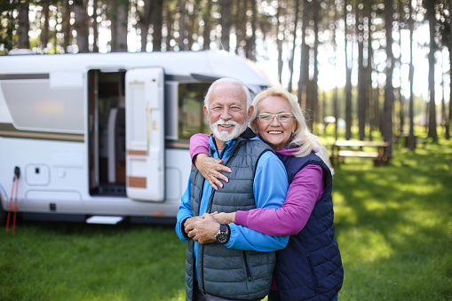 Senior couple camping in a forest with a recreational vehicle (motor home). Both about 65 years old, Caucasian people.