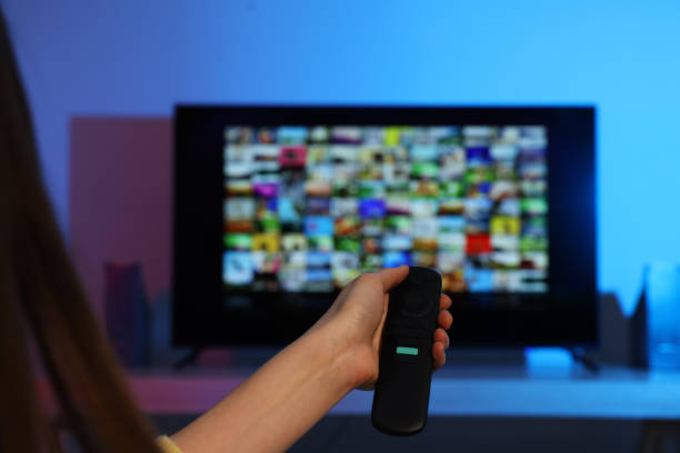 Woman switching channels on TV set with remote control at home, closeup