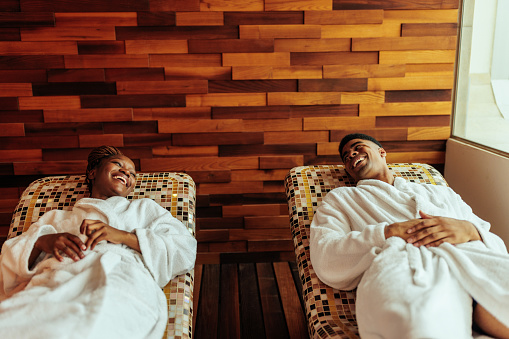 A young African American newlywed couple are on their honeymoon. They are staying in a luxurious hotel enjoying lying on the spa beds in the resort.