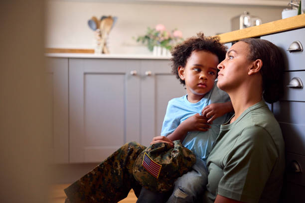 young son comforts depressed mother suffering with ptsd sitting on floor on home leave - depression sadness usa american flag imagens e fotografias de stock