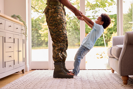 Close Up Of Loving Army Father In Uniform Home On Leave With Son Standing On Feet