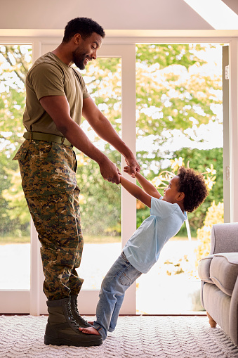 Loving Army Father In Uniform Home On Leave With Son Standing On Feet And Holding Hands