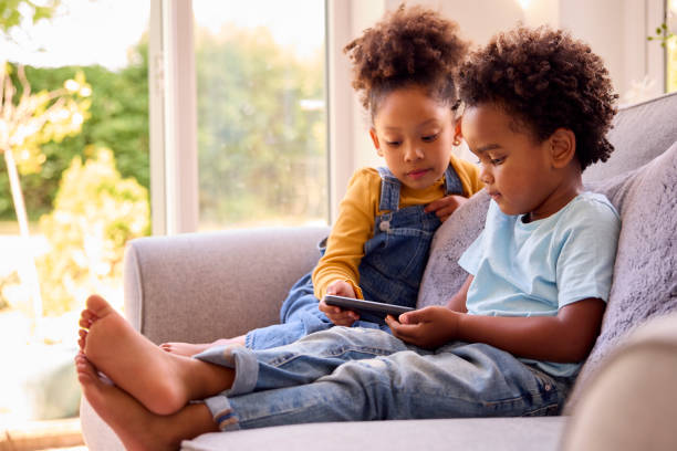 istock Boy And Girl Playing Handheld Computer Game Sitting On Sofa At Home Together 1428745473