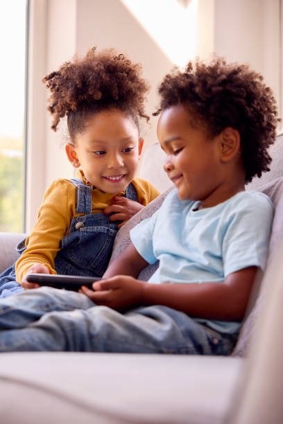 istock Boy And Girl Playing Handheld Computer Game Sitting On Sofa At Home Together 1428745539