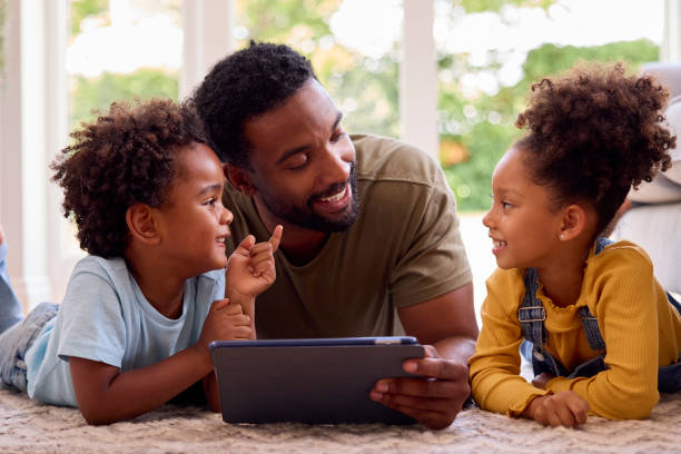 istock Father At Home Lying On Rug In Lounge With Children Using Digital Tablet 1428745735
