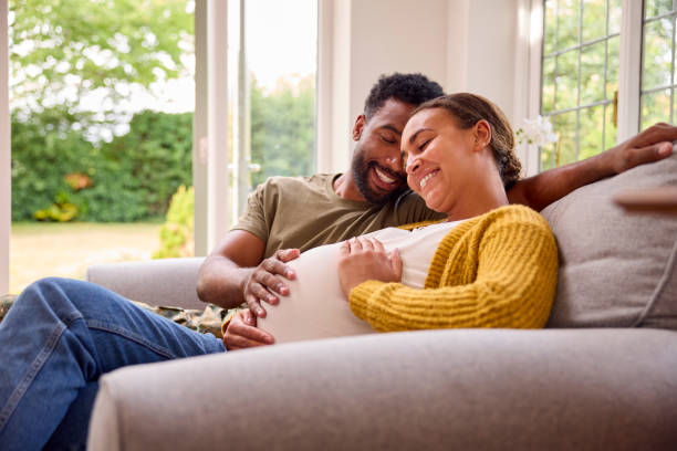Pregnant Couple With Woman Sitting Next To Army Husband In Uniform Home On Leave stock photo