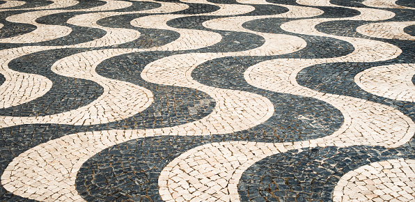 A distinctive black and white wave mosaic pattern on an outdoors tiled floor in Portugal.