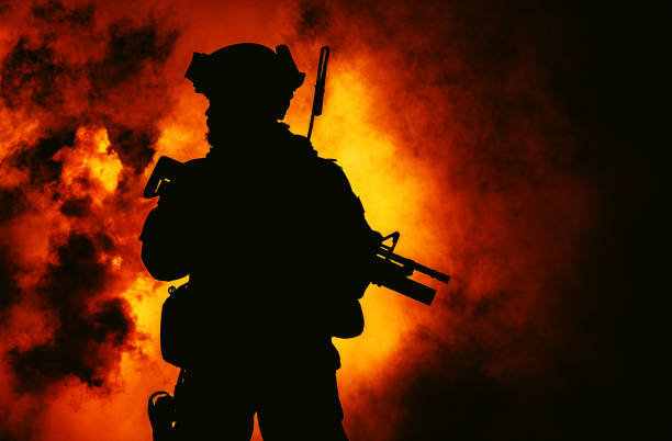 Silhouette of modern infantry soldier, elite army fighter in tactical ammunition and helmet, standing with assault service rifle in hands in the fire and smoke stock photo