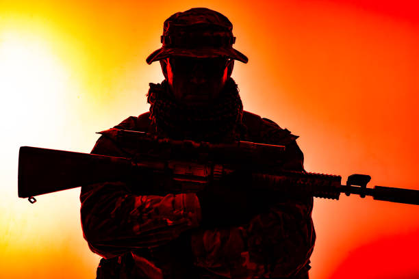 istock Army special forces soldier, commando shooter, mercenary in camouflage uniform, bonnie, hidden behind mask and glasses face, armed service rifle, low key, isolated studio shoot 1428747577