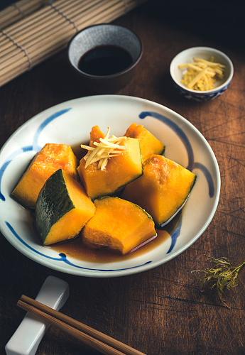 Autumnal  Kabocha Squash (Japanese Pumpkin) recipe. Japanese Simmered Kabocha cooked in savory dashi broth seasoned with soy sauce and sake with pumpkin seeds, close up, wooden rustic background. Autumn and winter hot Japanese recipe