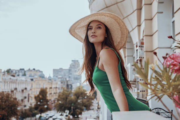 istock Attractive young woman adjusting her elegant hat and looking at view while standing on the balcony 1428749361