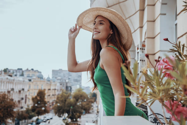 istock Happy young woman adjusting her elegant hat and looking at view while standing on the balcony 1428749368
