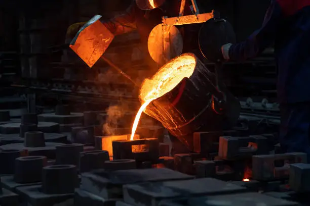 Photo of Liquid metal or cast iron poured into molds. Metal casting process with red high temperature fire in metallurgical factory. Metal part factory, foundry cast, heavy industry