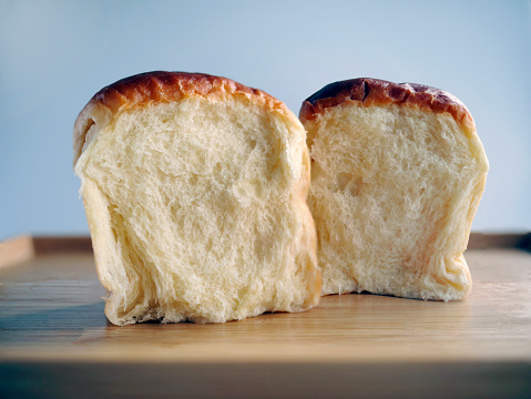 Close up showing the cross section, 2 buns of Fresh baked Japanese Hokkaido soft and fluffy milk bread, Japanese Brioche on the wooden tray with plain background, warm tone