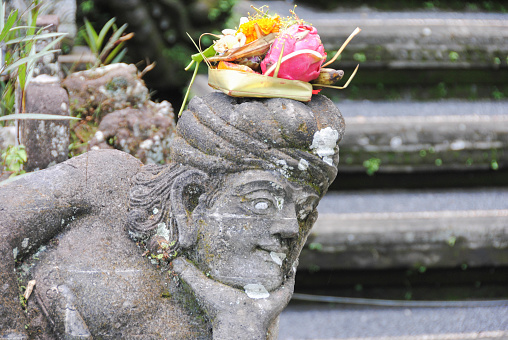 Balinese religious offering (canang sari) over a stone statue.