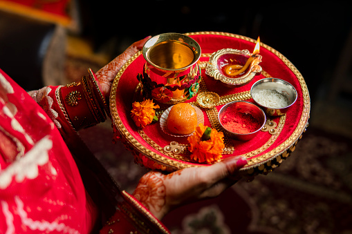 Tradition Indian woman holding a plate decorated with oil lamp, sweet food, flowers, and religious offering on the occasion of Karwa Chauth festival.