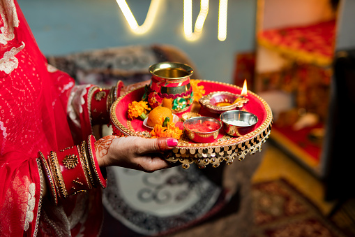 Tradition Indian woman holding a plate decorated with oil lamp, sweet food, flowers, and religious offering on the occasion of Karwa Chauth festival.