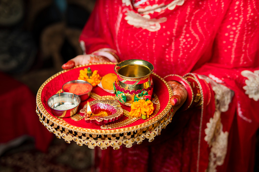 Tradition Indian woman holding a plate decorated with oil lamp, sweet food, flowers, and religious offering on the occasion of Karwa Chauth festival.