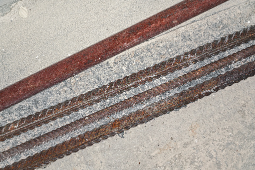Iron rusty construction rebars on concrete ground at building site closeup detail from above.