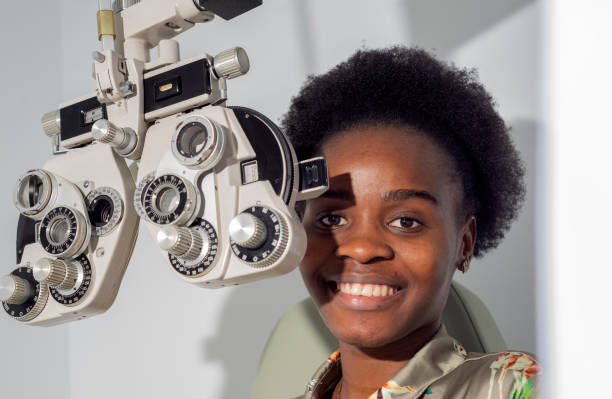 African young woman girl doing eye test checking examination in clinic or optical shop, sitting at phoropter equipment. Eyecare concept. stock photo