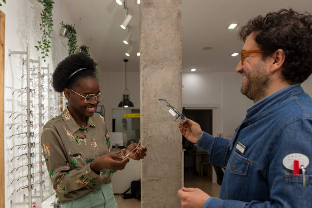 Smiling optician shows glasses to young African customer stock photo