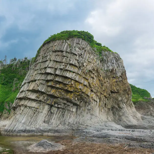 coastal landscape, beautiful columnar basalt cliff on the wooded coast of Kunashir island