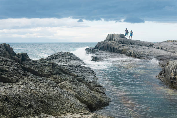 przybrzeżny pejzaż morski z pięknymi kolumnowymi skałami bazaltowymi podczas odpływu, turyści są widziani w oddali w rozmyciu - kunashir island zdjęcia i obrazy z banku zdjęć