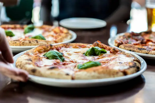 Photo of Close up view of a Margherita Neapolitan style pizza with buffalo mozzarella, tomato sauce and basil - Waiter hand serving pizza at pizza restaurant