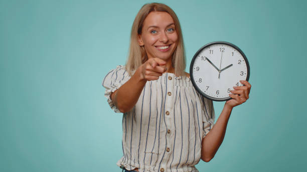 charmante jeune femme montrant l’heure sur la montre de l’horloge, ok, pouce levé, approuver, pointer du doigt l’appareil photo - vérifier lheure photos et images de collection