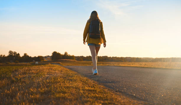 istock Woman with backpack walks along the road on the sunset. 1428774065