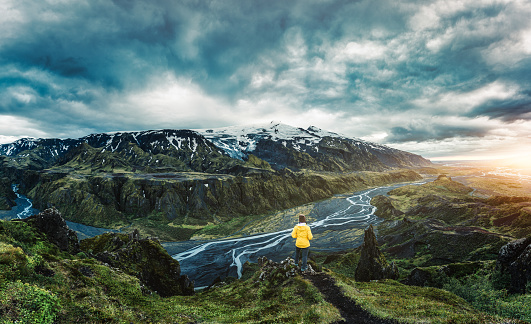 Panorama dramatic view of hiker standing on top of Valahnukur viewpoint among the volcanic mountain and Krossa river in Icelandic Highlands on summer at Thorsmork, Iceland