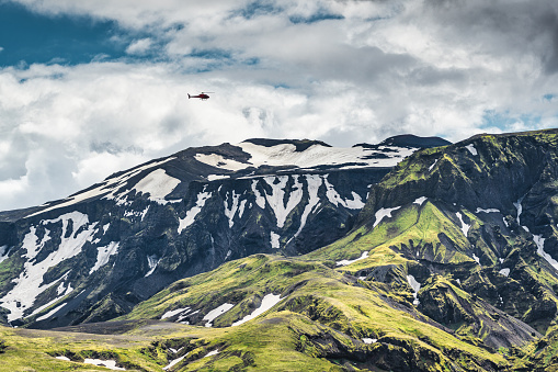 Majestic green mountain canyon with snow covered and helicopter flying above in Icelandic Highlands on summer at Thorsmork, Iceland