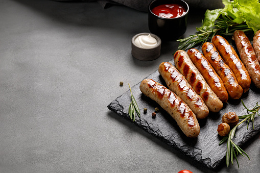 Barbecue sausages on a stone board and dark background. Grilled sausages with rosemary, copy space.