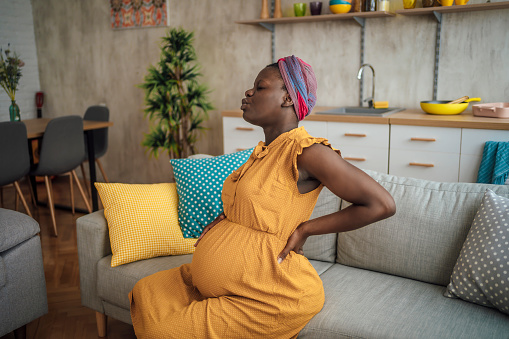 Young pregnant woman experiencing contractions while sitting on the sofa at home