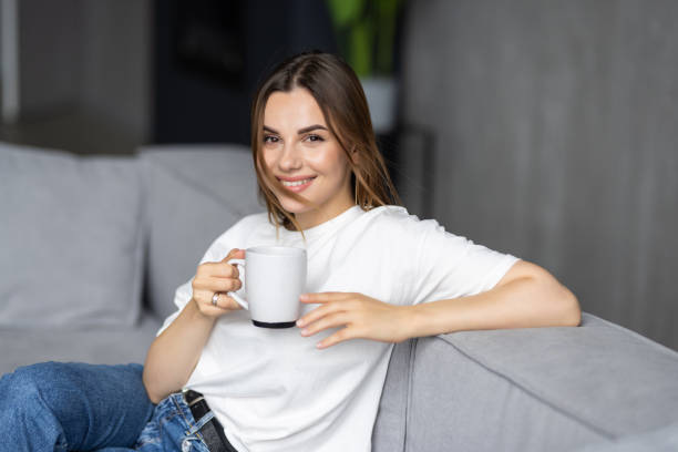 istock Young woman sitting on couch at home and drinking coffee 1428779383