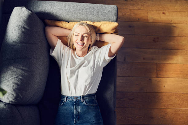 Laughing adult woman lying on the sofa at home relaxing with eyes closed stock photo