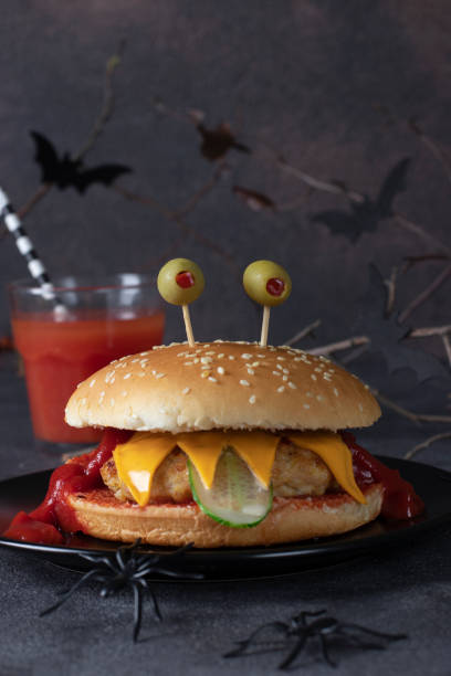 Funny monster chicken burger with toast cheese, ketchup, olives and cucumber on dark background. Creative Halloween food stock photo