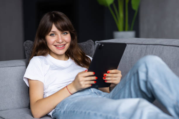 istock Young woman using tablet sitting on sofa at home at living room. 1428792290