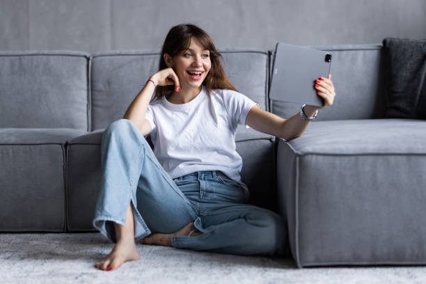 istock Beautiful young woman using a digital tablet and smiling while sitting on couch at home 1428793423