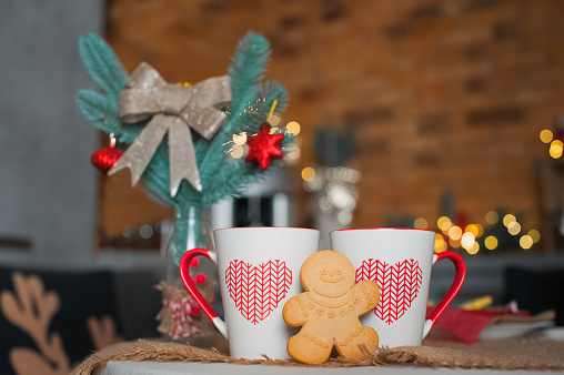 Two cups and gingerbread men on table with garlands blurred background. Kitchen is decorated for New Year. Interior details with Christmas decor.