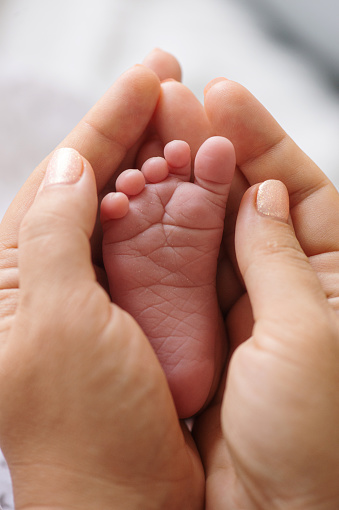 Tiny foot of a newborn baby in the mother's palms.  Mom holds a newborn baby's foot in her hands.  Close-up of a newborn baby's foot. Mother loves her baby. The concept of motherhood and parenthood