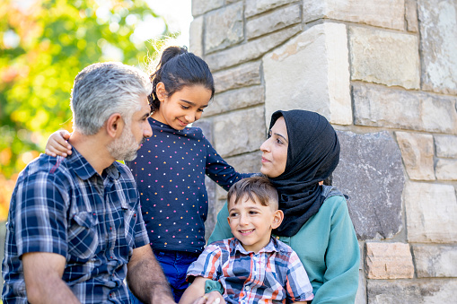 A small Middle Eastern family of four spend time bonding together in their new country after immigrating to Canada.  They are each dresed casually and the mother has a Hijab on as they laugh and spend quality time together.
