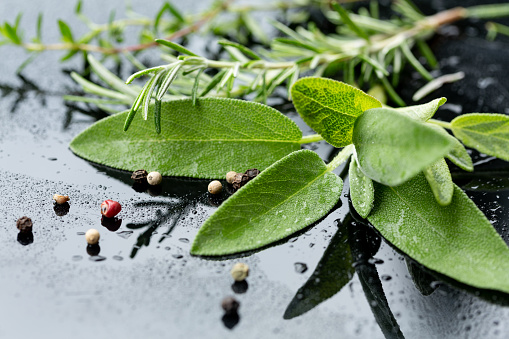 close up of sage leaves, rosemary and peppercorns on black background