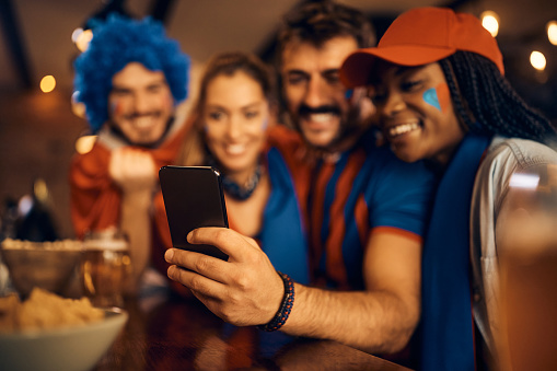 Close up of sports fans watching football match via live stream on mobile phone in bar.