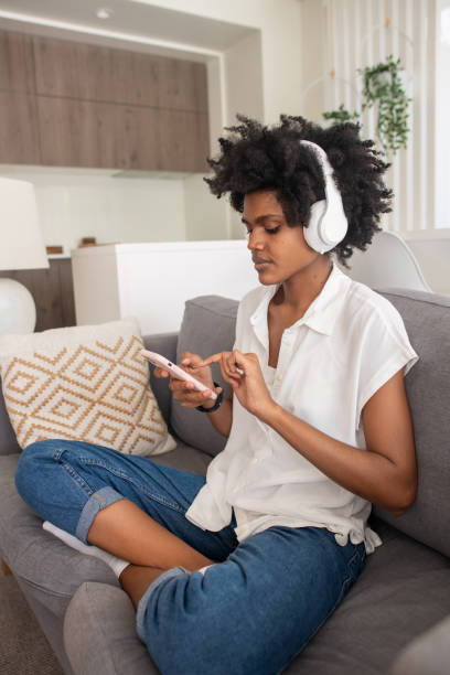 istock Woman in headphones sitting on sofa and using phone 1428805092