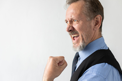 Close-up of excited mature businessman celebrating success. Senior Caucasian manager wearing formalwear looking away and showing fist against white background. Success and triumph concept