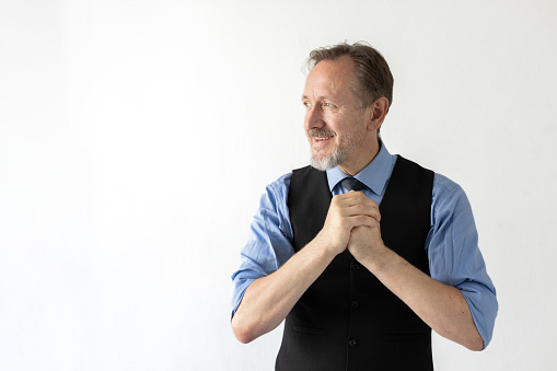 Portrait of happy mature businessman clasping hands and looking away. Senior Caucasian manager wearing formalwear smiling against white background. Successful businessman concept