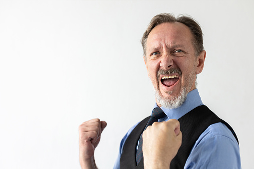 Portrait of happy mature businessman making winning gesture and shouting against white background. Senior Caucasian manager wearing formalwear celebrating success. Success and triumph concept