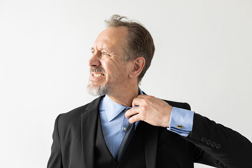 Portrait of irritated mature businessman pulling shirt and clenching teeth. Displeased senior Caucasian manager unbuttoning tight shirt collar. Uncomfortable clothing or overworking concept